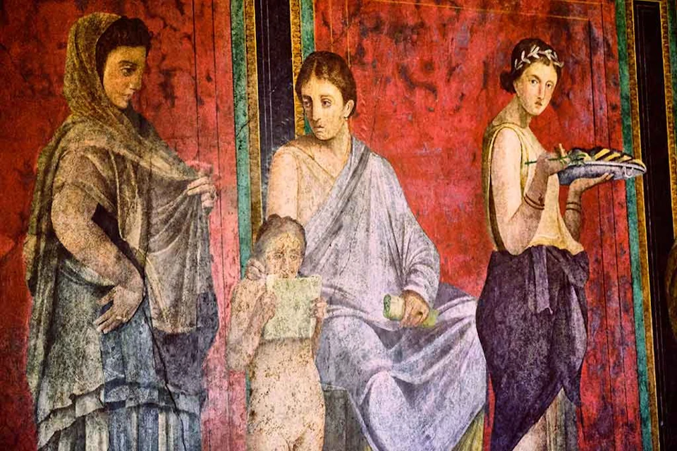 A fresco depicting three figures: a seated man, a standing woman holding a tray, and a child reading a scroll, against a red background.