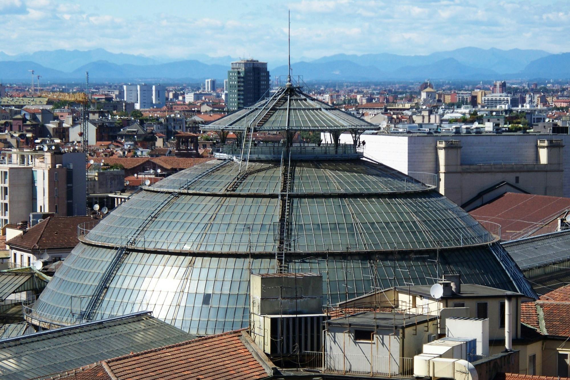 Ein Panoramablick auf eine Stadtlandschaft mit einer großen Glaskuppel im Vordergrund und Bergen im Hintergrund.