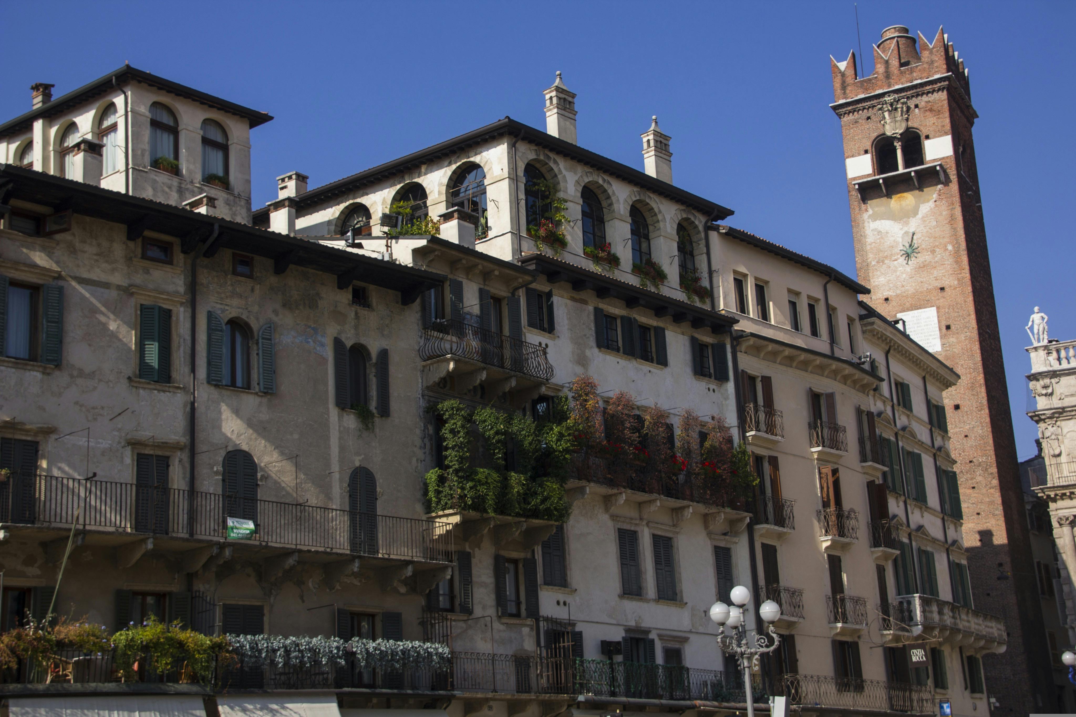 Historic European buildings with balconies adorned with plants and flowers under a clear blue sky.