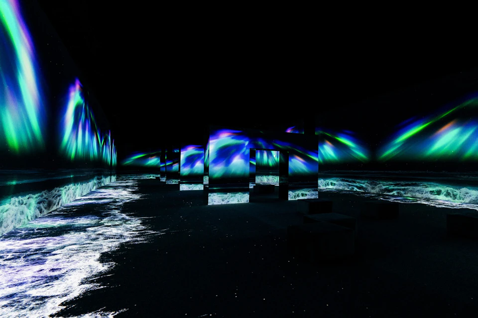 A dark room with mirrors reflecting blue and green aurora-like lights and a floor partly covered in white, wave-like patterns.