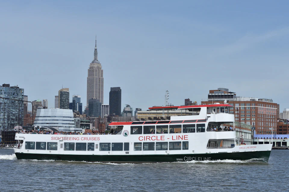 A sightseeing cruise boat labeled "Circle Line" in the water with the New York City skyline, including the Empire State Building, in the background.