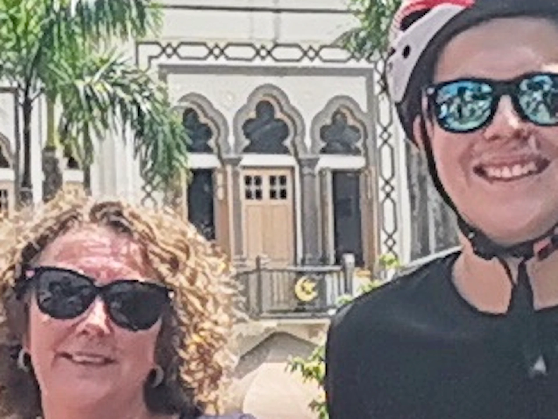Five people with bicycles stand on a cobblestone street lined with colorful buildings and palm trees, with a golden-domed structure visible.