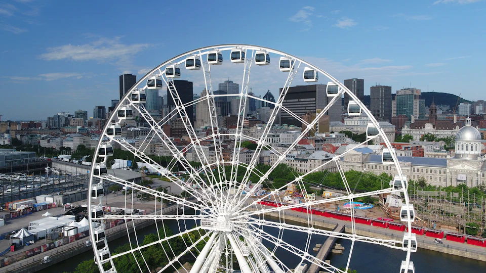 A large Ferris wheel in the foreground with a city skyline of tall buildings and clear blue sky in the background.