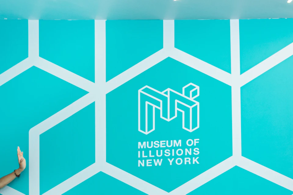 Two people in a geometric room at the Museum of Illusions New York, creating an optical illusion of size difference.