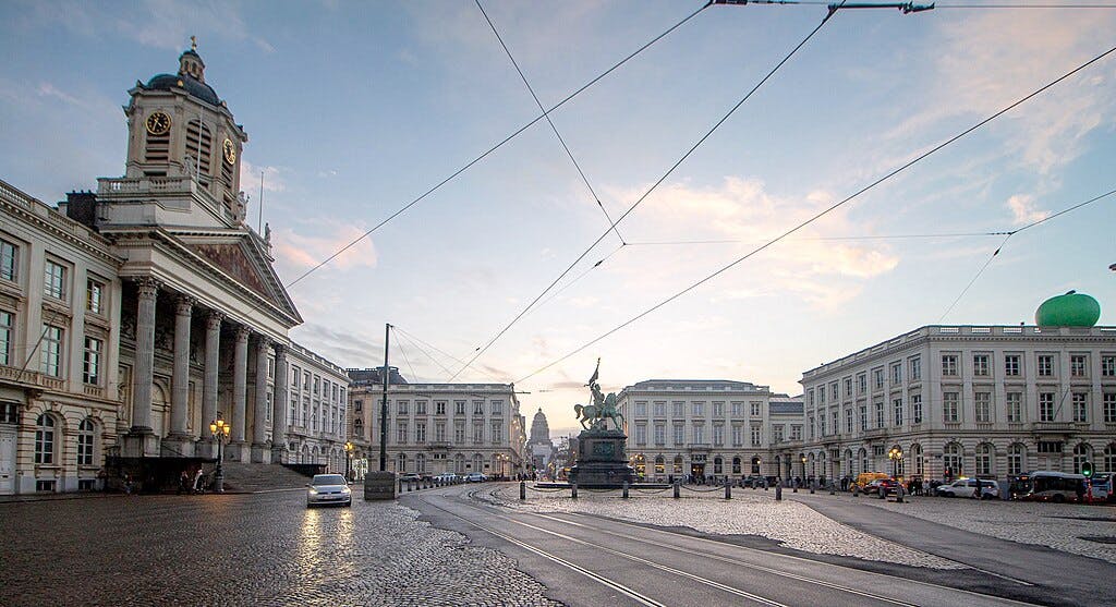 Una amplia plaza adoquinada con edificios históricos alrededor, una estatua ecuestre central y escaso tráfico bajo un cielo crepuscular.