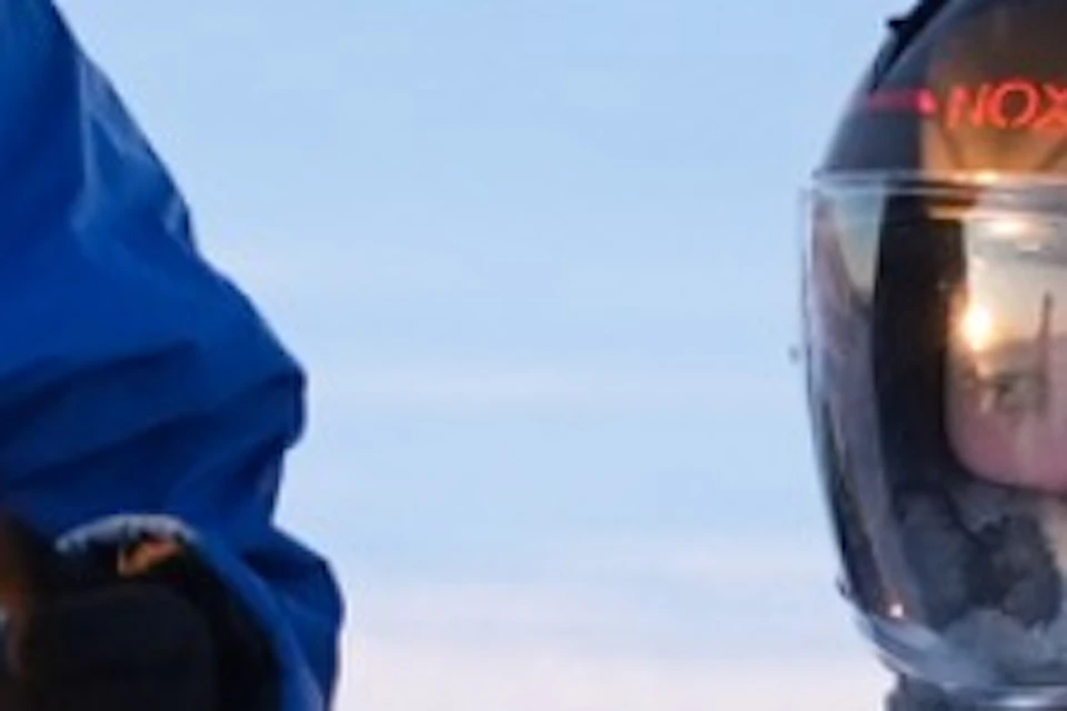 A group of people wearing helmets sitting on snowmobiles in a snowy landscape during sunset.