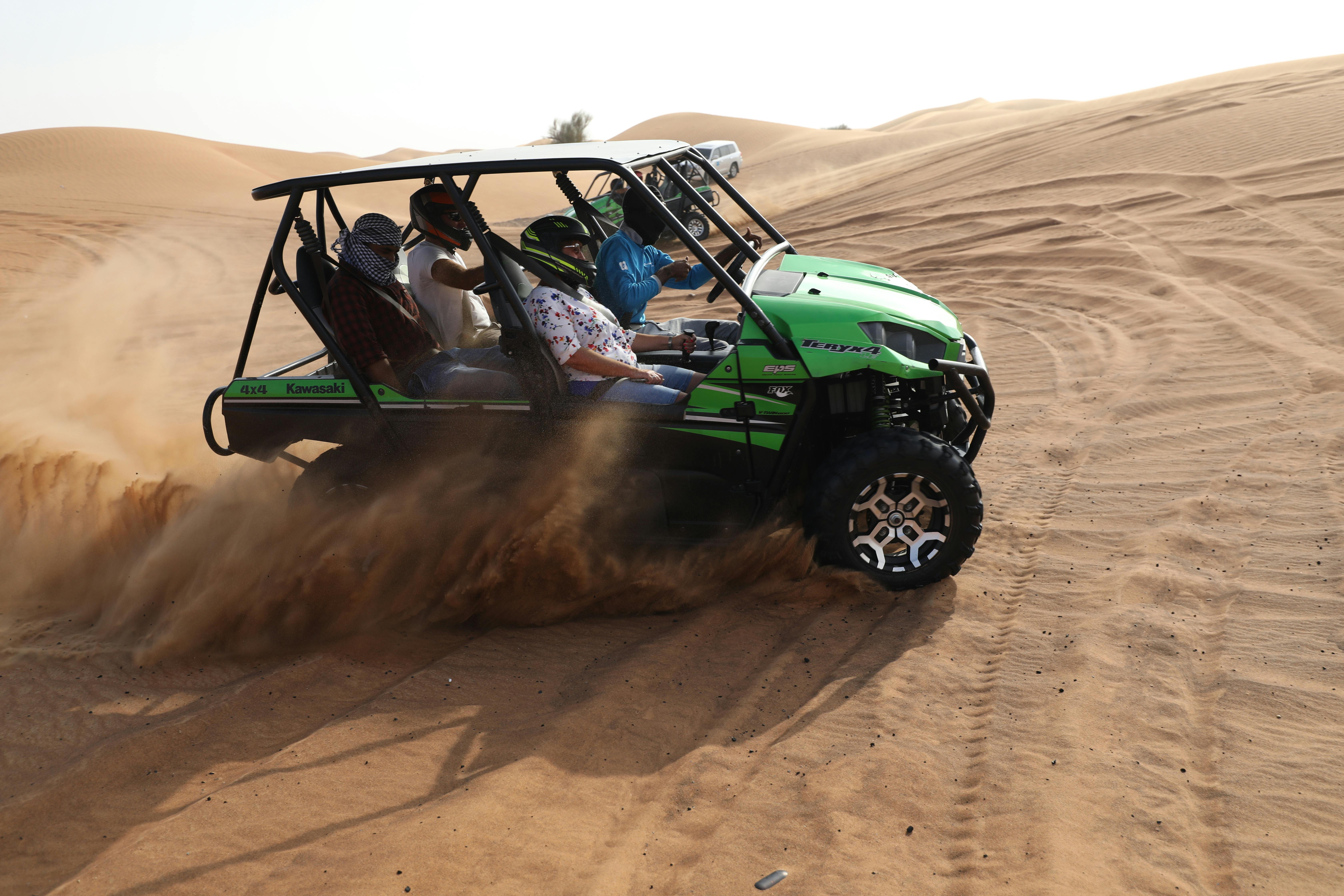 Quattro persone in sella a un fuoristrada verde sfrecciano tra le dune sabbiose del deserto.