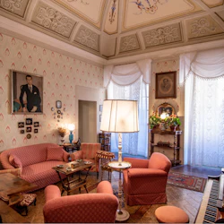 Ett vintage vardagsrum med utsmyckat tak, mönstrade tapeter, rosa stoppade möbler, olika målningar och ett piano.