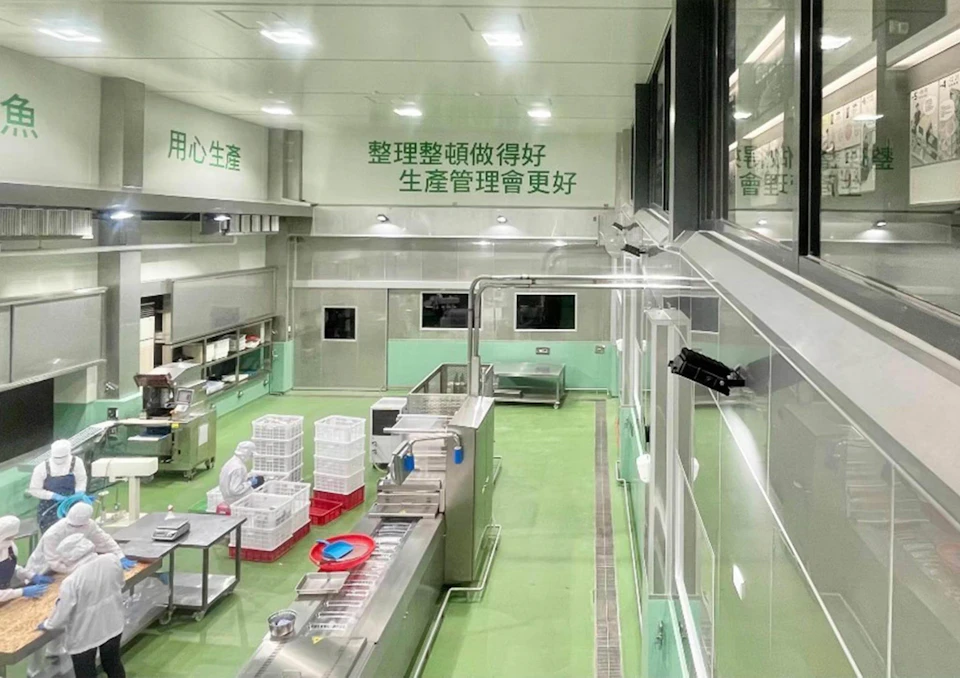 A clean and organized industrial workspace with green and white walls, stainless steel equipment, and labeled storage bins.