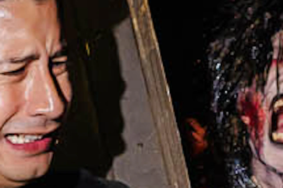 A man reacts in fright as actors dressed as zombies reach toward him in a haunted house-themed setting.