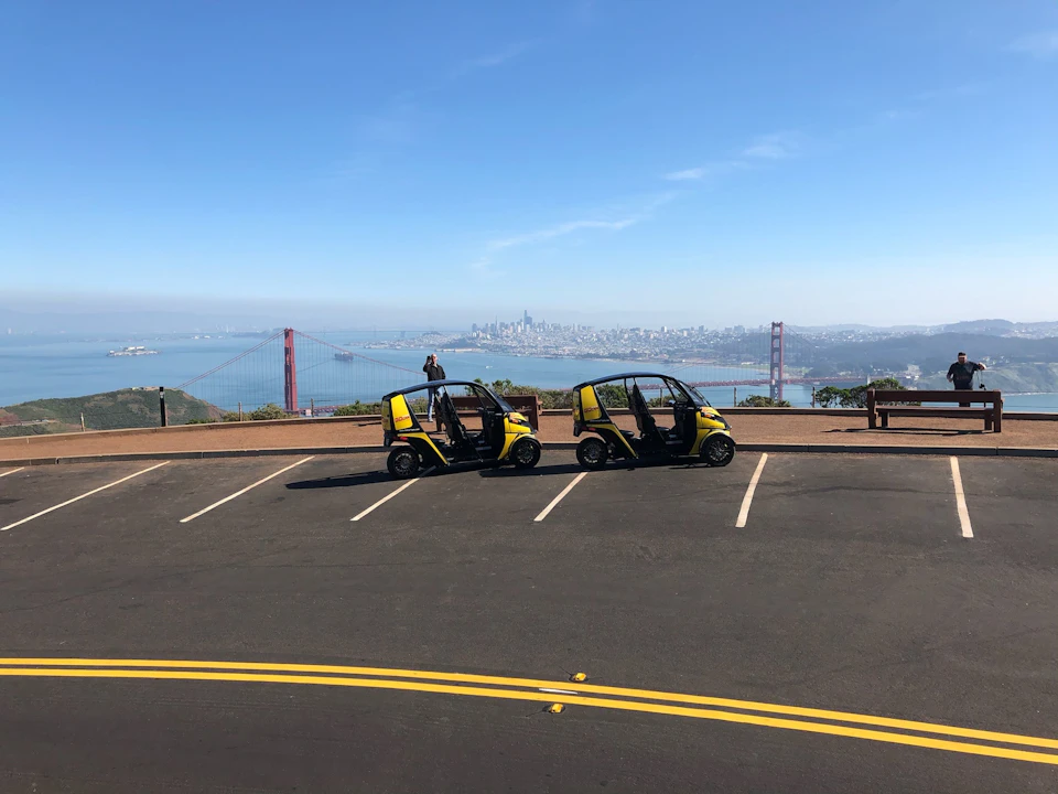 Two small yellow electric vehicles parked in a scenic spot overlooking the Golden Gate Bridge and San Francisco skyline.