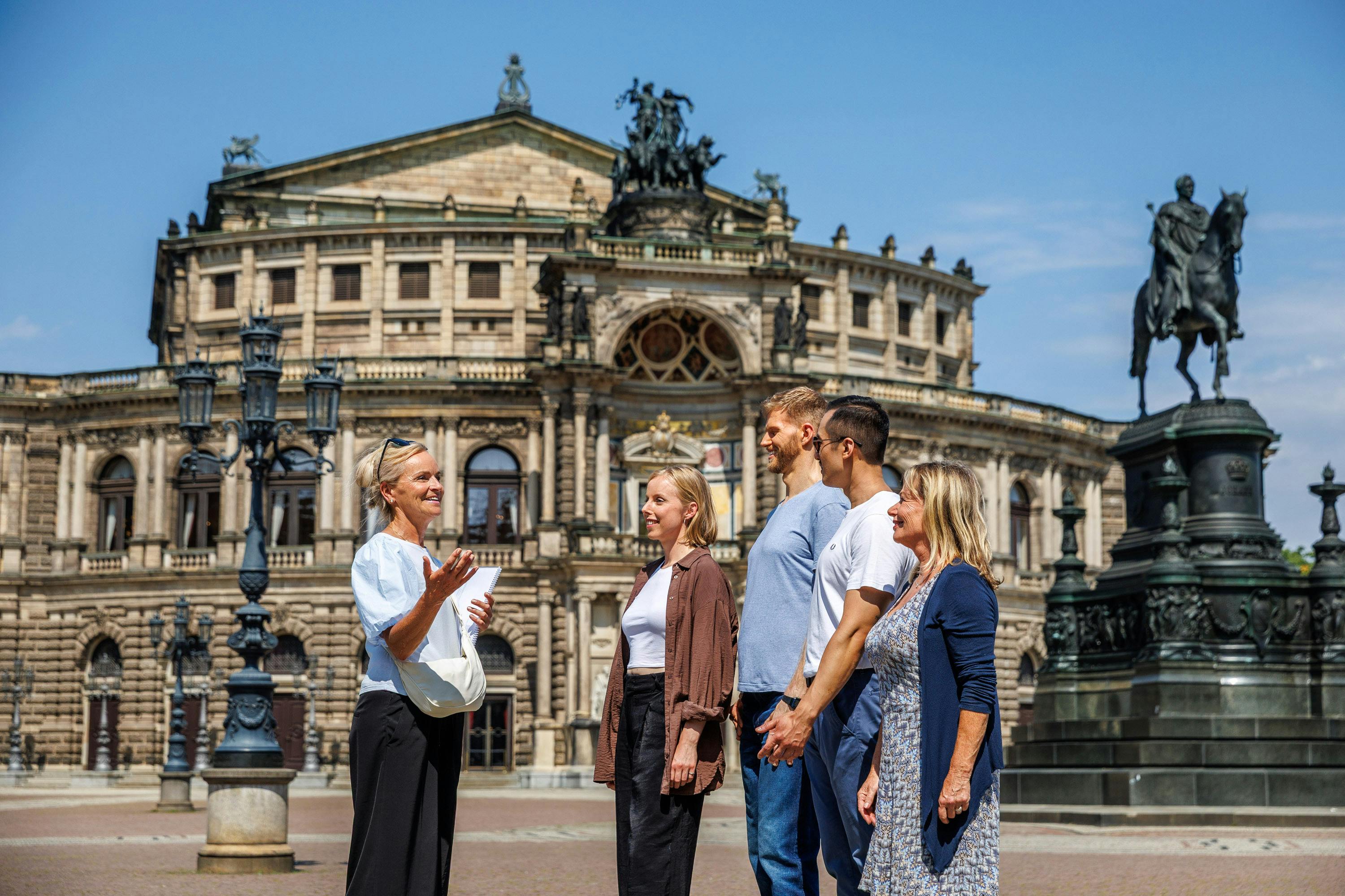Un grup de persones davant d'un edifici històric amb una arquitectura ornamentada i un cel blau clar.