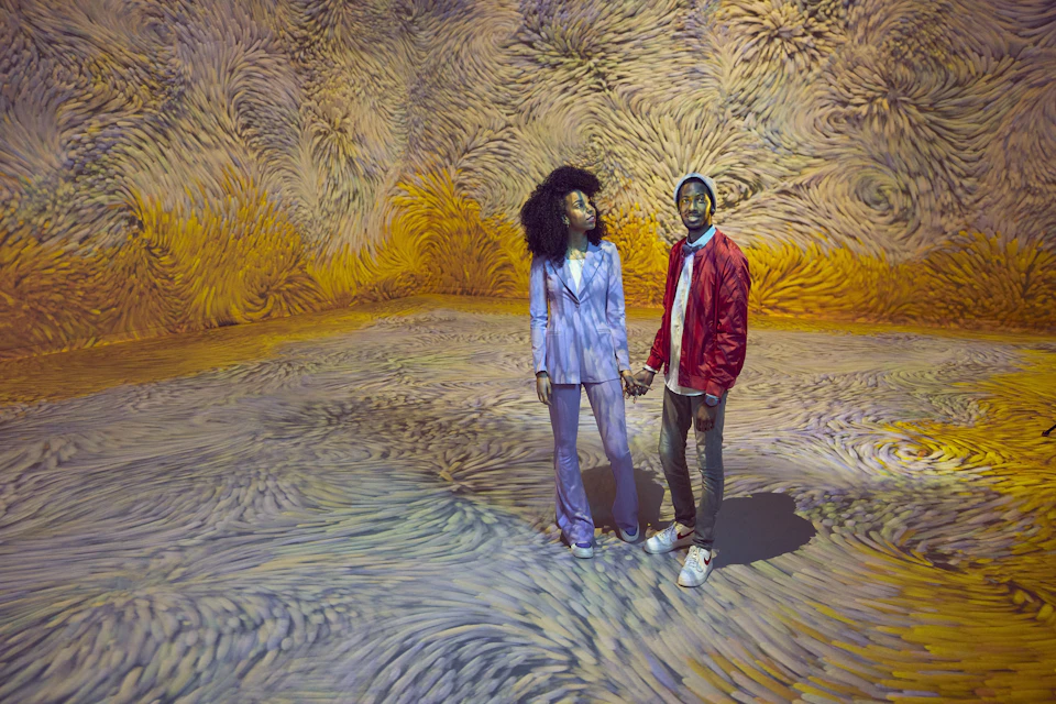 Two people holding hands in a room with swirling, colorful patterns on the walls and floor.