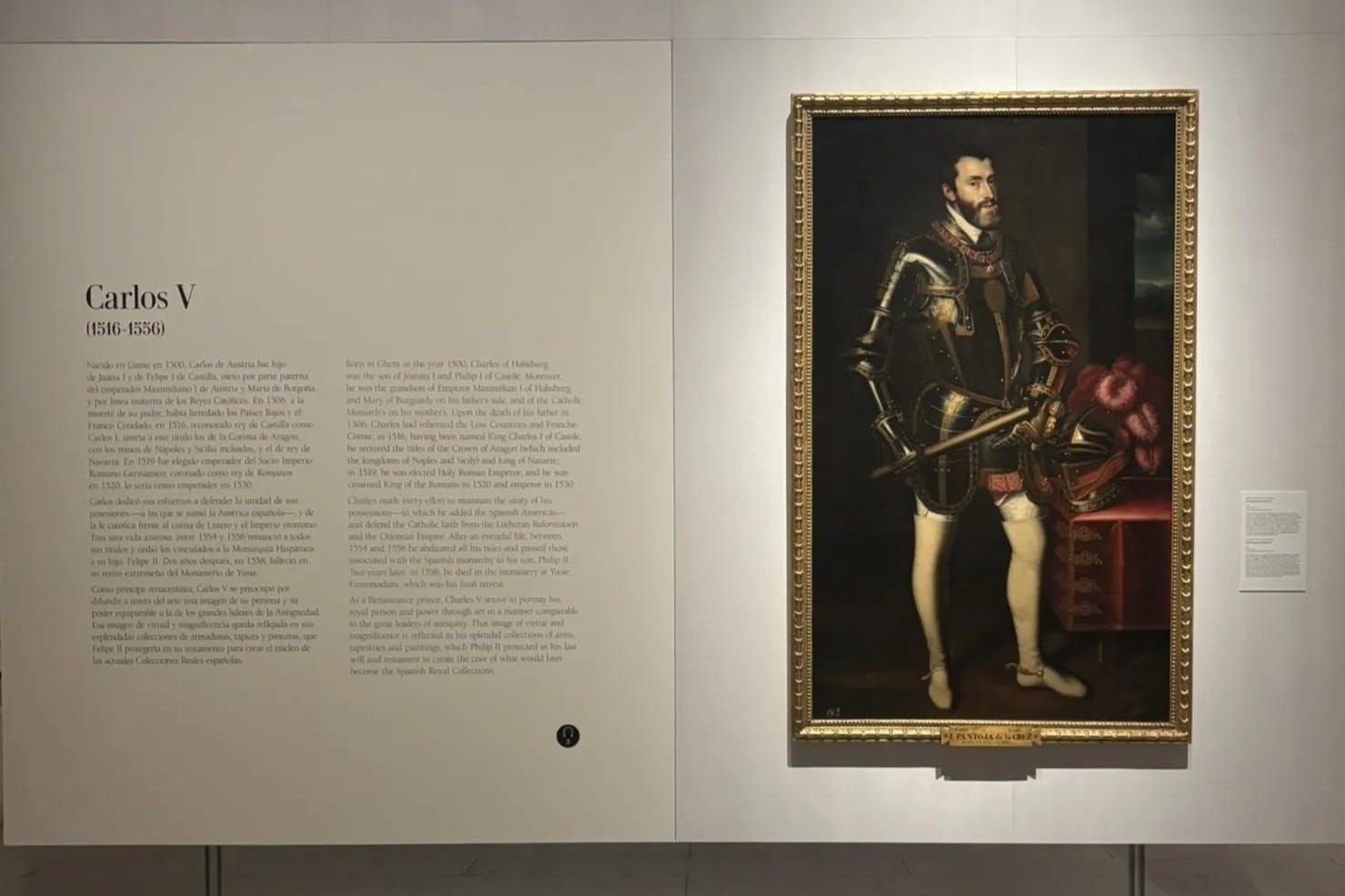 美術館のギャラリーに展示されている、鎧を着た剣を持った男の額絵。壁には記述的な銘板が貼られている。