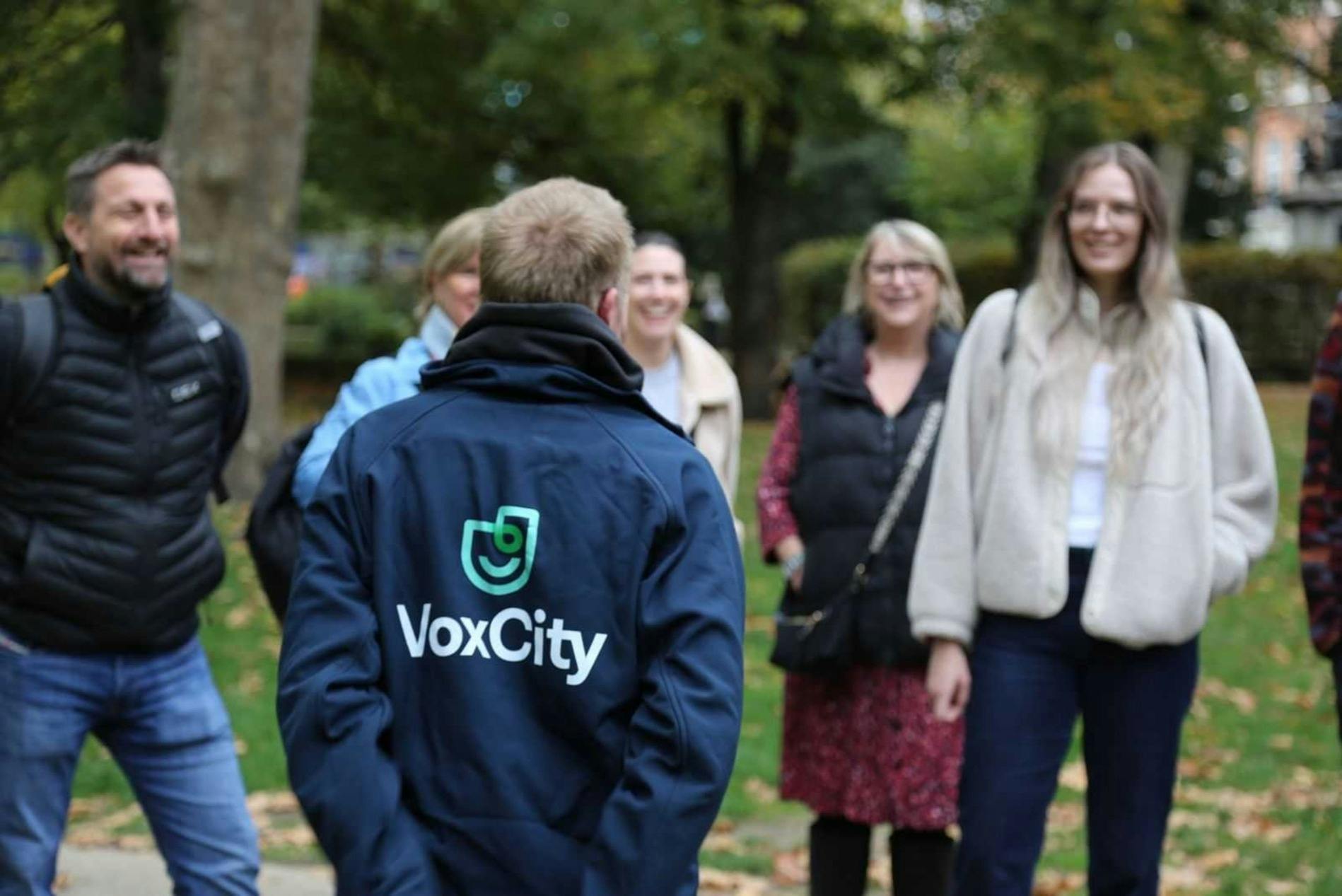 屋外にいる人々のグループ、1人は背中に「boxCity」のジャケットを着ていて、他の人は笑顔で、木々が後ろにある草の上に立っています。