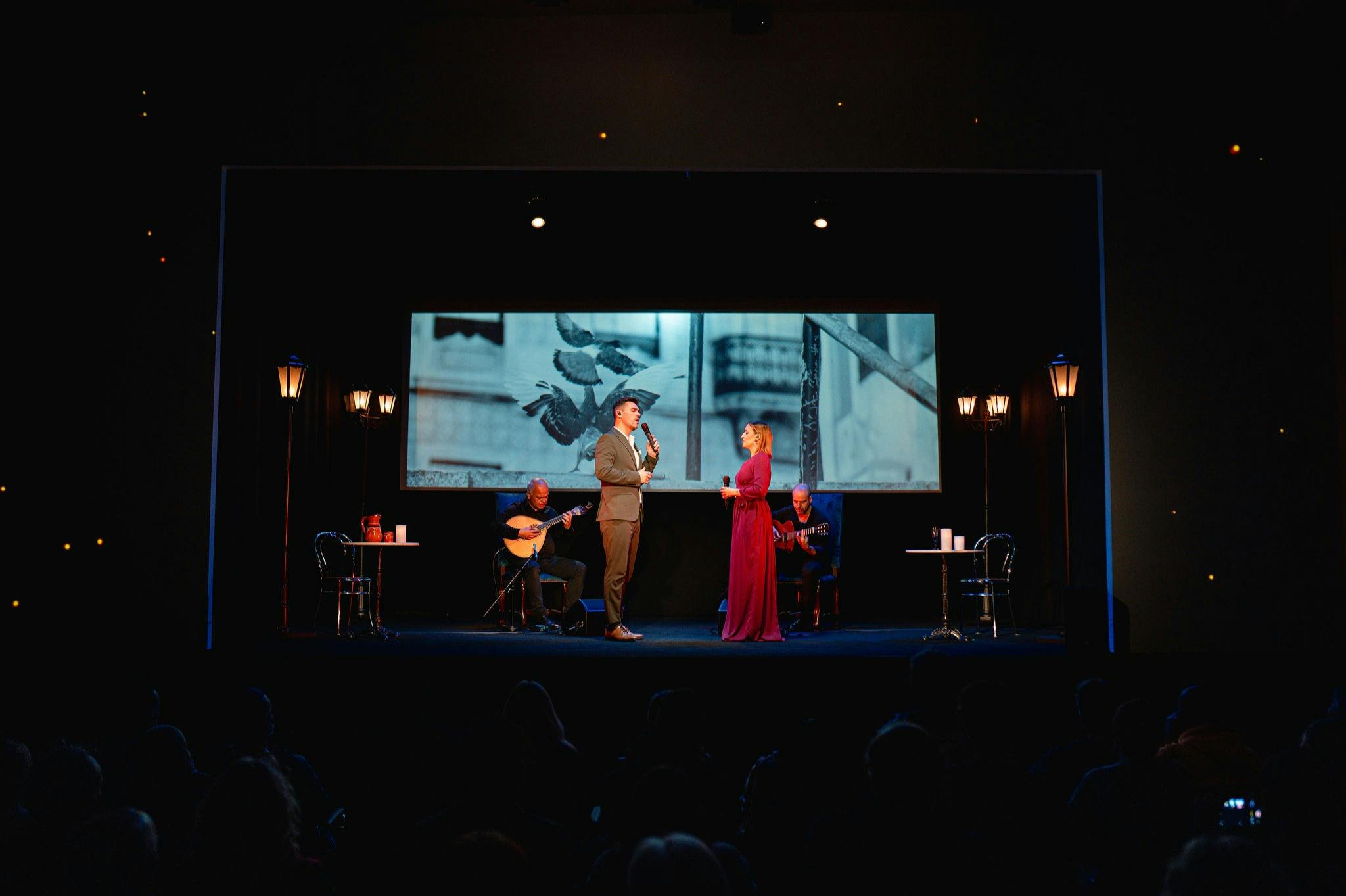 2人の俳優が、鳥を背景にした薄暗いステージで演奏します。 ステージの両側でギターを弾く2人のミュージシャン。