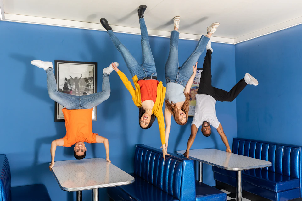 Four people hanging upside-down from a ceiling in a blue diner with booths and tables attached to the floor.
