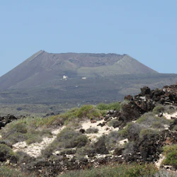 Distant view of a mountain with a flat summit and dry vegetation in the foreground, under a clear blue sky.