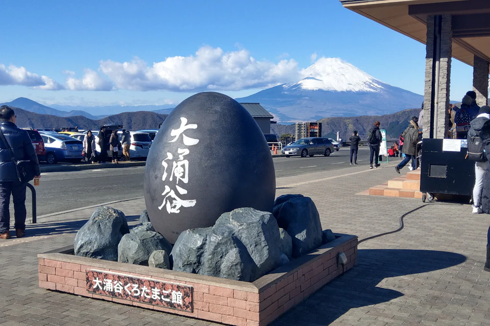 A large black egg sculpture with Japanese text, surrounded by rocks, with Mount Fuji visible in the background.
