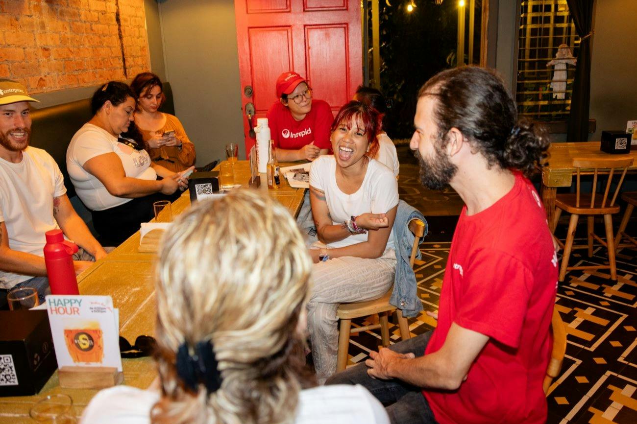 A group of people seated around a table in a casual indoor setting, having a lively conversation and sharing drinks.