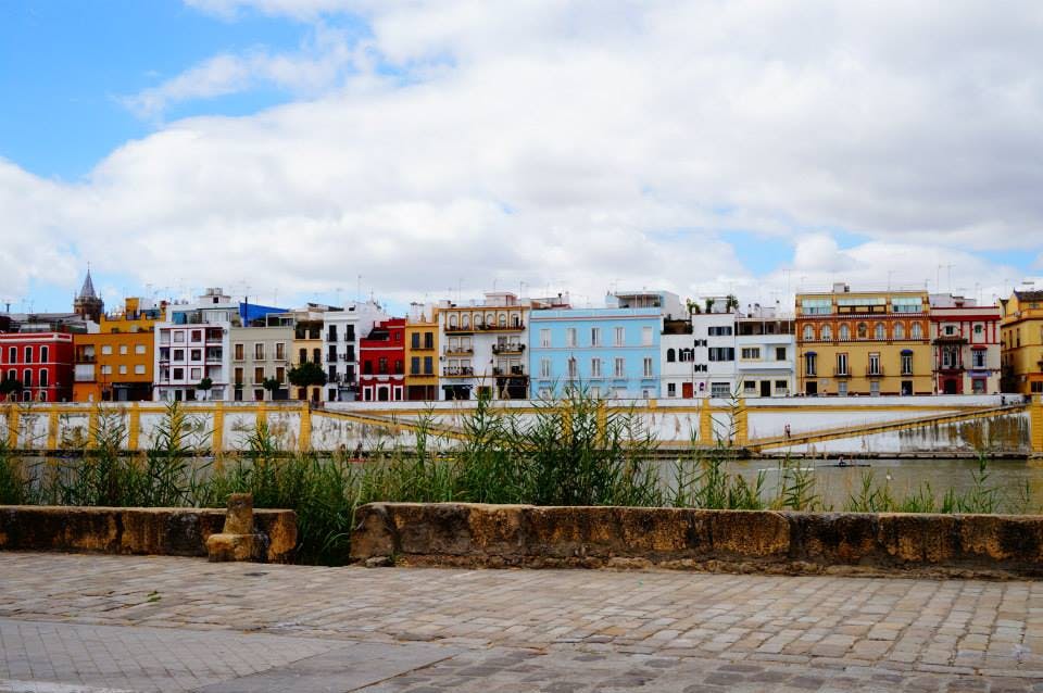 Fila di edifici colorati sotto un cielo nuvoloso, con muro di pietra ed erba in primo piano.
