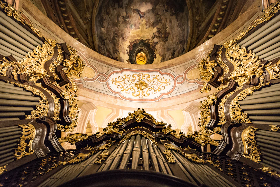 Ornate church interior with a richly decorated pipe organ, detailed gold embellishments, and a frescoed domed ceiling.