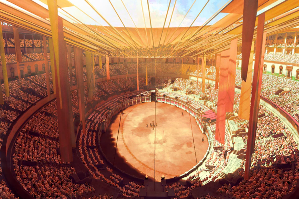 A sunlit, packed stadium with a large circular arena in the center, surrounded by tiered seating and adorned with orange banners.
