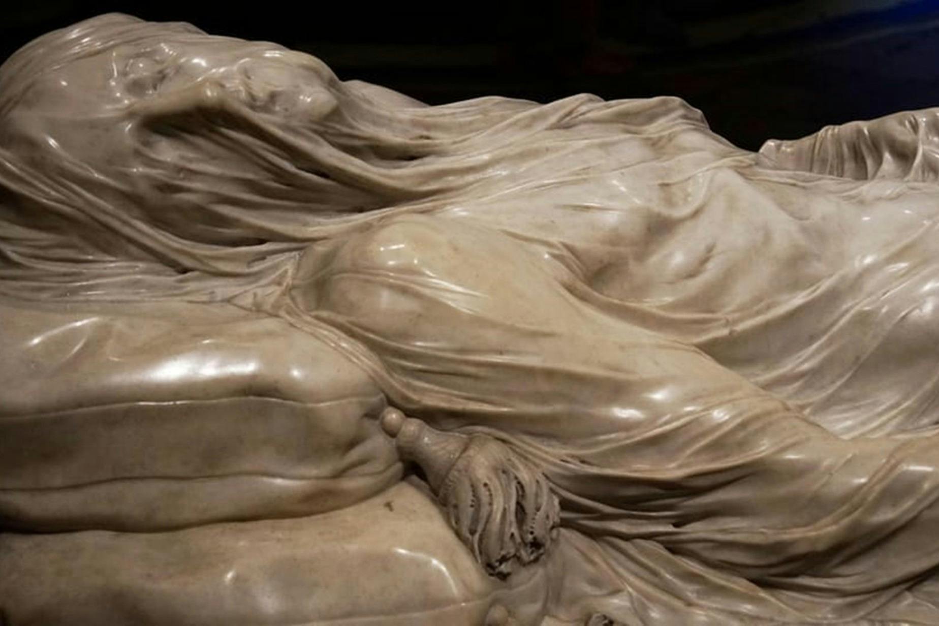 Primer pla d'una escultura de marbre que representa un teixit drapejat i detalls intrincats d'una mà que sosté un objecte.