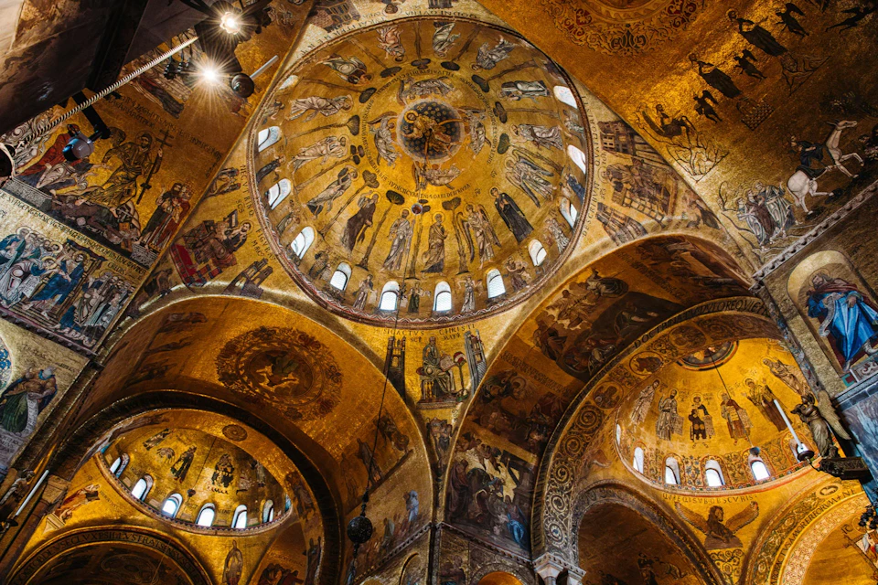 Elaborate golden mosaics on a domed ceiling, depicting religious figures and intricate patterns, in a historic building.
