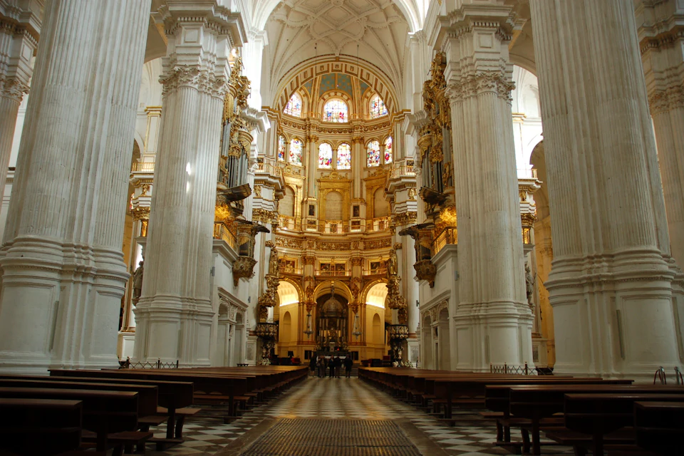 Interior of a grand cathedral with high vaulted ceilings, ornate columns, and stained glass windows.