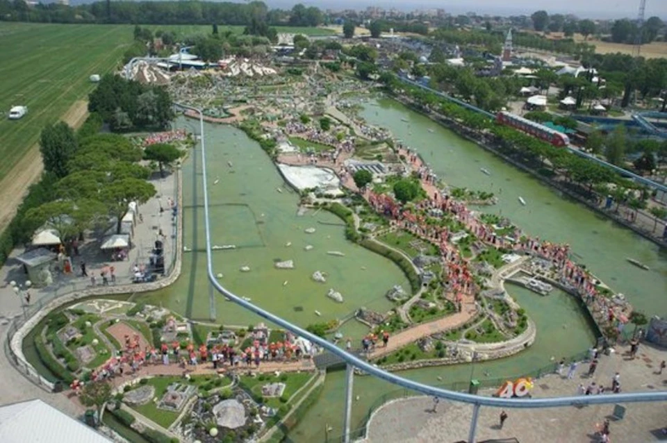 Aerial view of a large miniature park with detailed scale models, pathways, green spaces, and water features, crowded with visitors.