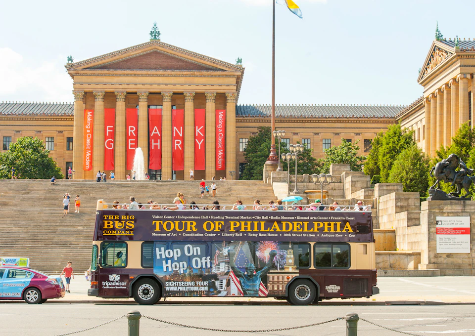 A double-decker bus promoting a Philadelphia tour is parked in front of the Philadelphia Museum of Art, with the "FRANK GEHRY" banner visible.