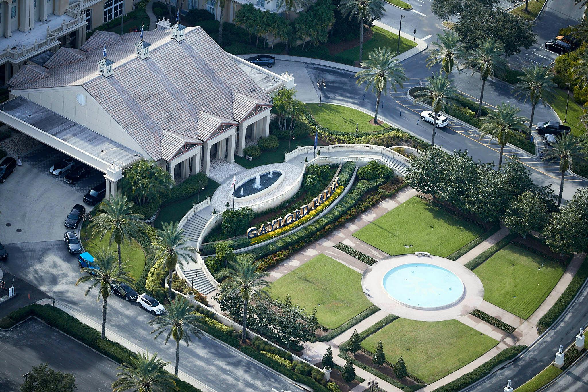 Letecký pohled na vstup do rezortu Gaylord Palms s fontánou, upravenými zahradami a okolními silnicemi a zaparkovanými auty.