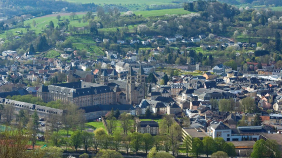 Aerial view of a historic European town surrounded by green fields and trees, featuring a prominent church and rooftops.
