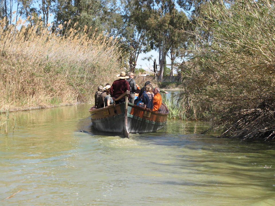 A group of people in a wooden boat navigating through a narrow waterway bordered by tall grasses and trees.