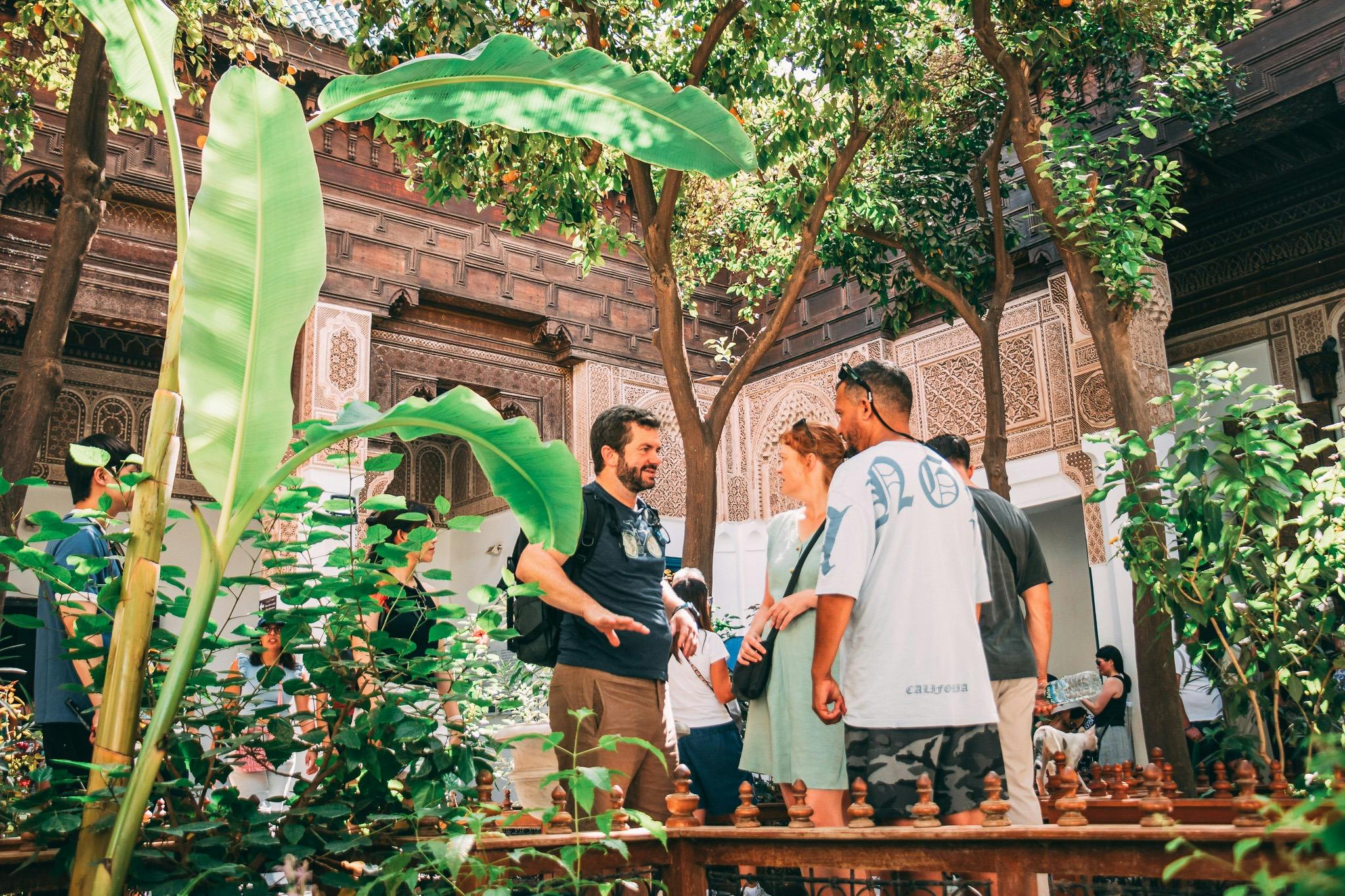 A group of people conversing in a courtyard with lush greenery and ornate wooden architecture.