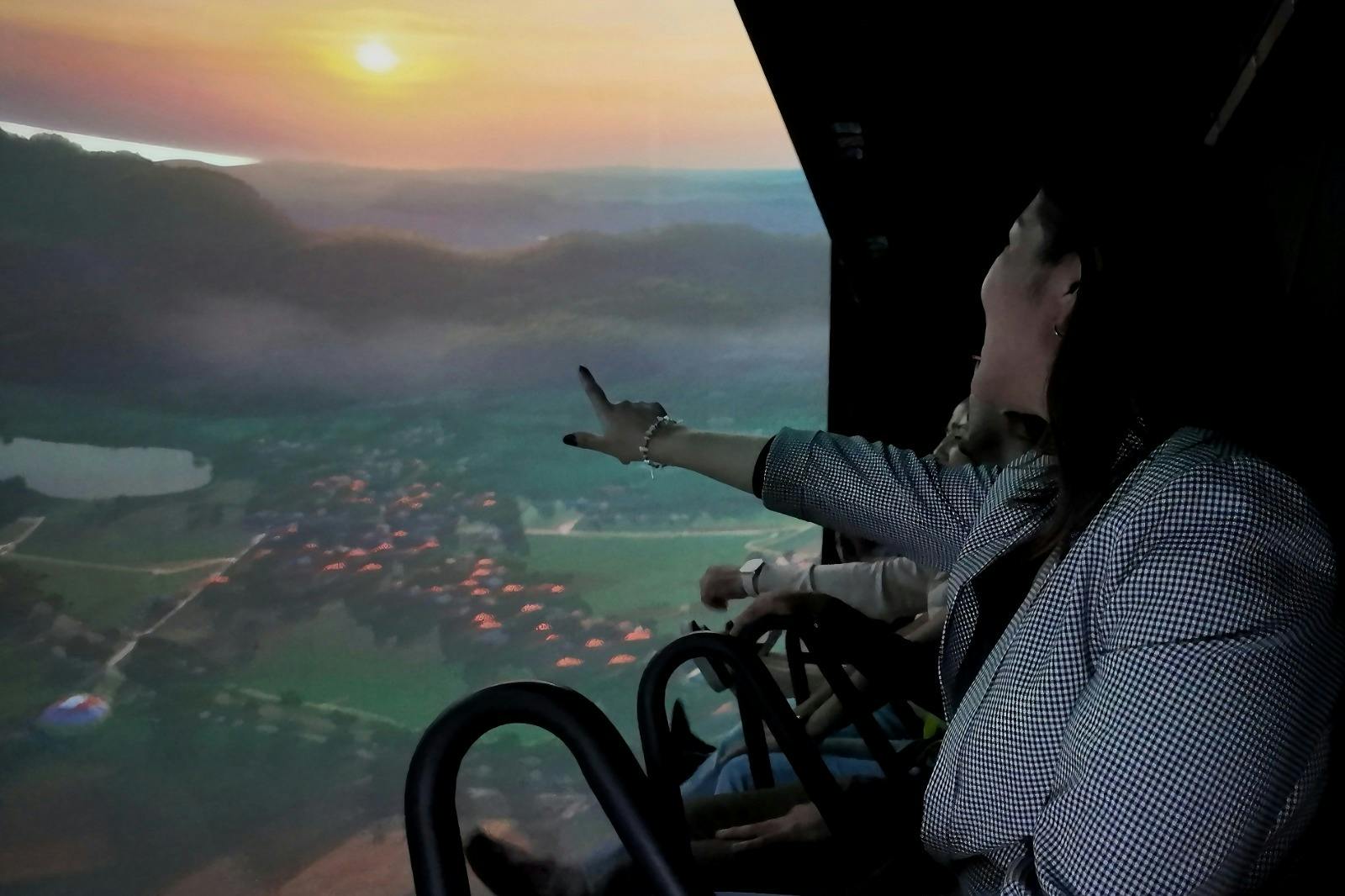 パノラマスクリーンの乗り物に座って、夕日の景色を眺める人々。 スクリーンに向かって指差す女性。