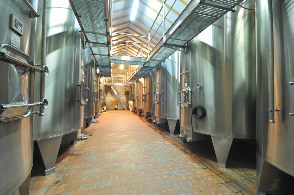 A large industrial hall with several stainless steel tanks and overhead walkways, lit by ceiling lights.