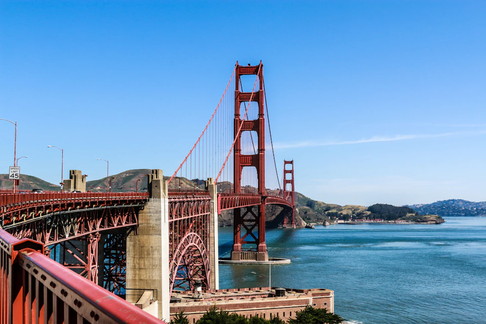 The Golden Gate Bridge stretches over blue water with hills and a clear sky in the background.