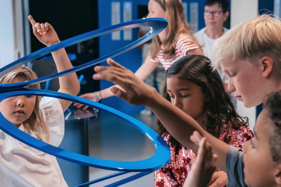 Children interacting with a blue spiral exhibit in a science museum, engaging and pointing at the structure.