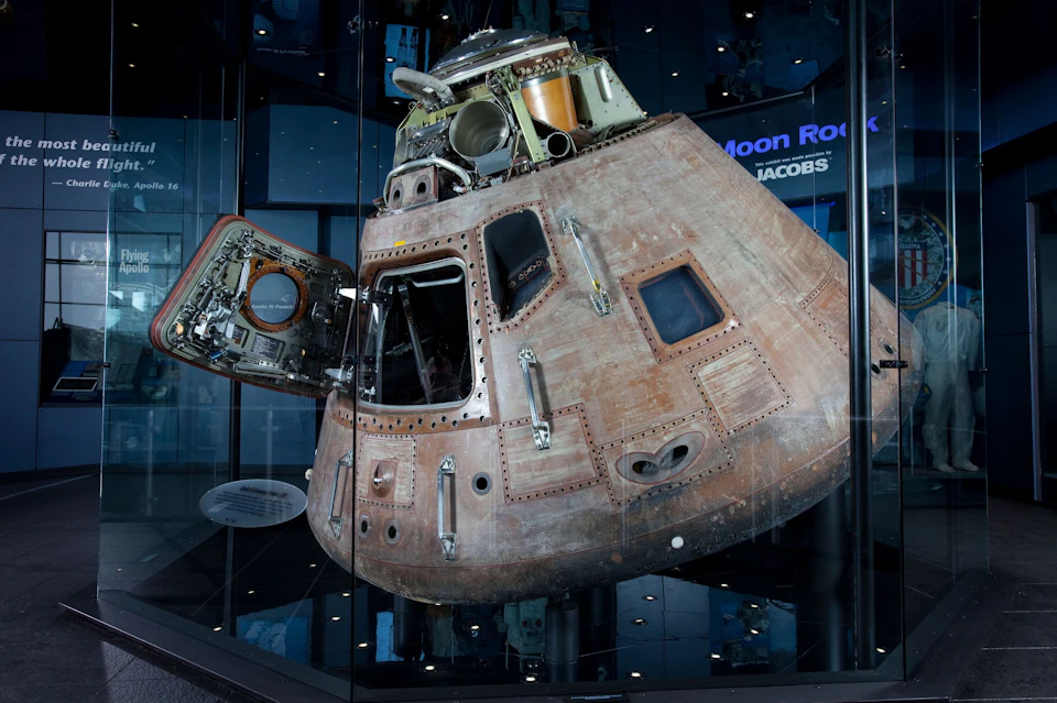 Apollo command module displayed in a museum exhibit, encased in glass with part of the module door open.