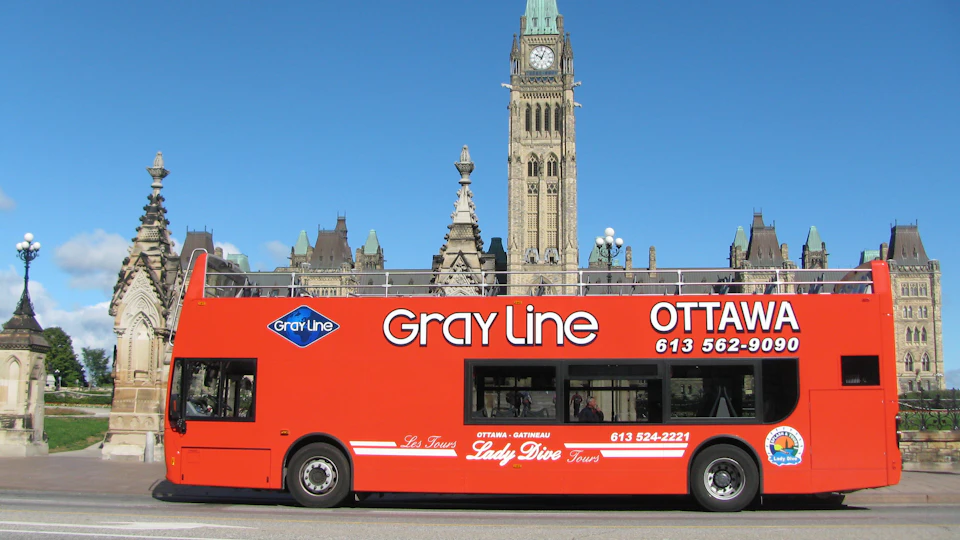A bright red double-decker tour bus with "Gray Line" branding, in front of historic Parliament buildings.