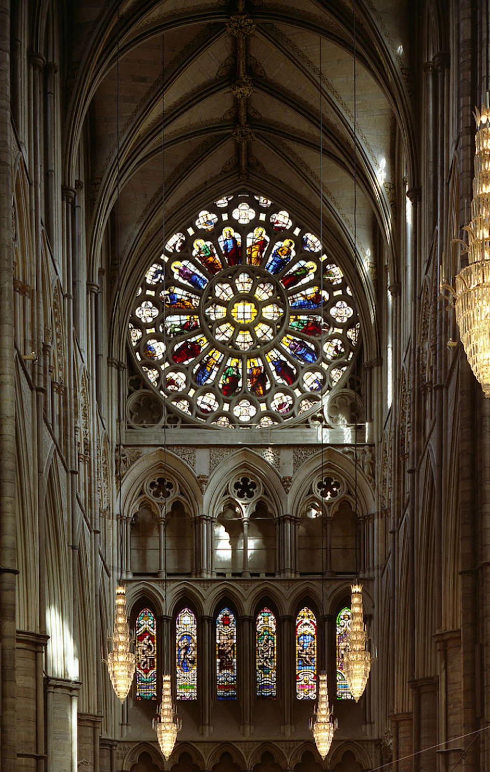 Cathedral interior featuring elaborate stained glass rose window, pointed arches, and a large chandelier on the right.