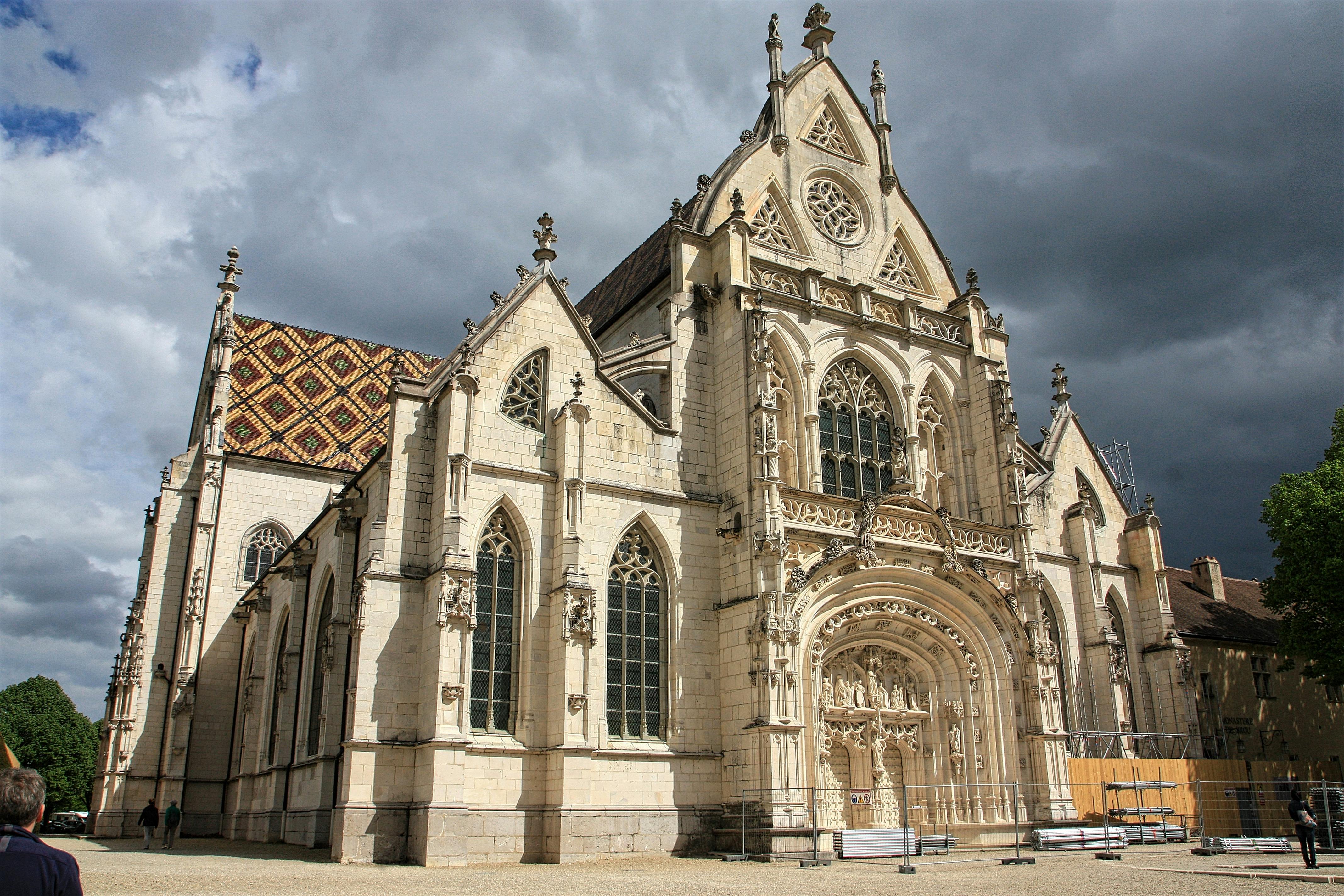 Gothic-style cathedral with ornate stone facade, arched windows, and detailed carvings against a cloudy sky backdrop.