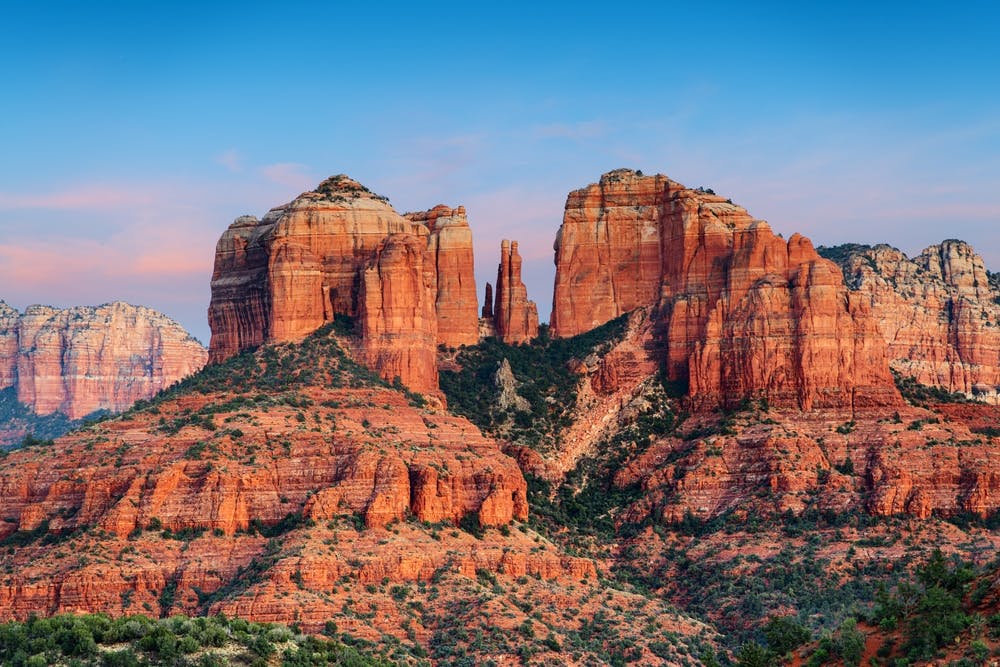 Red rock formations and plateaus with sparse green vegetation under a clear blue sky at sunset.
