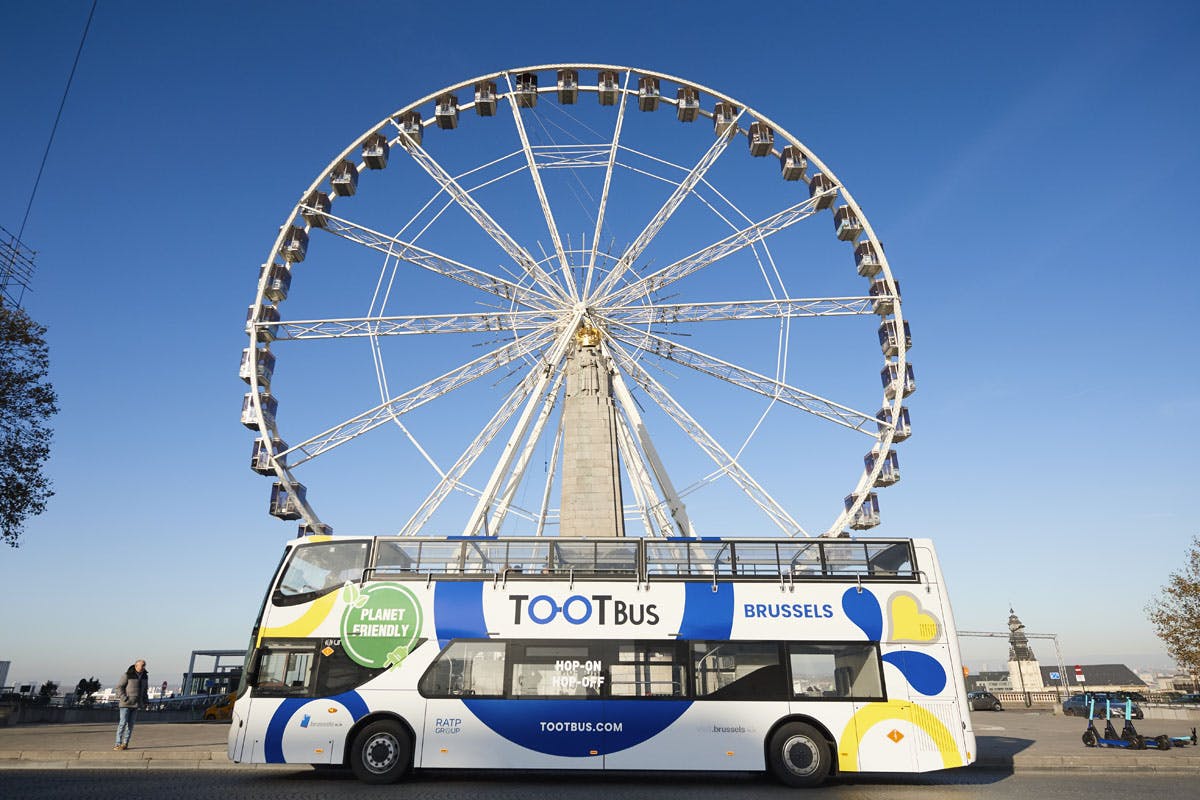 Autobus turistico a due piani a Bruxelles in sosta con una grande ruota panoramica sullo sfondo sotto un cielo azzurro e limpido.