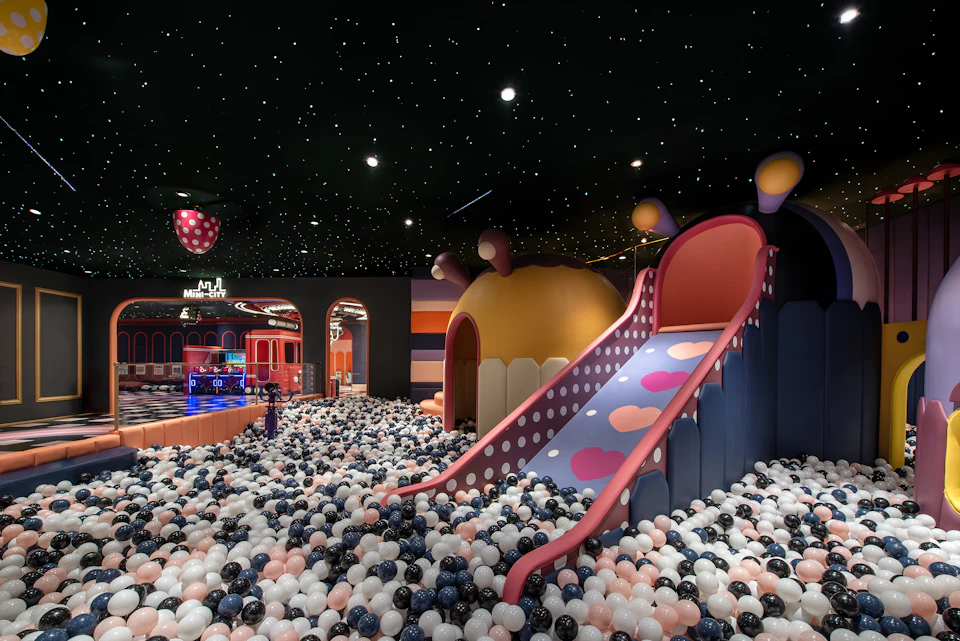 Indoor children's play area with colorful slides, dome-shaped structures, and a ball pit under a ceiling of star-like lights.