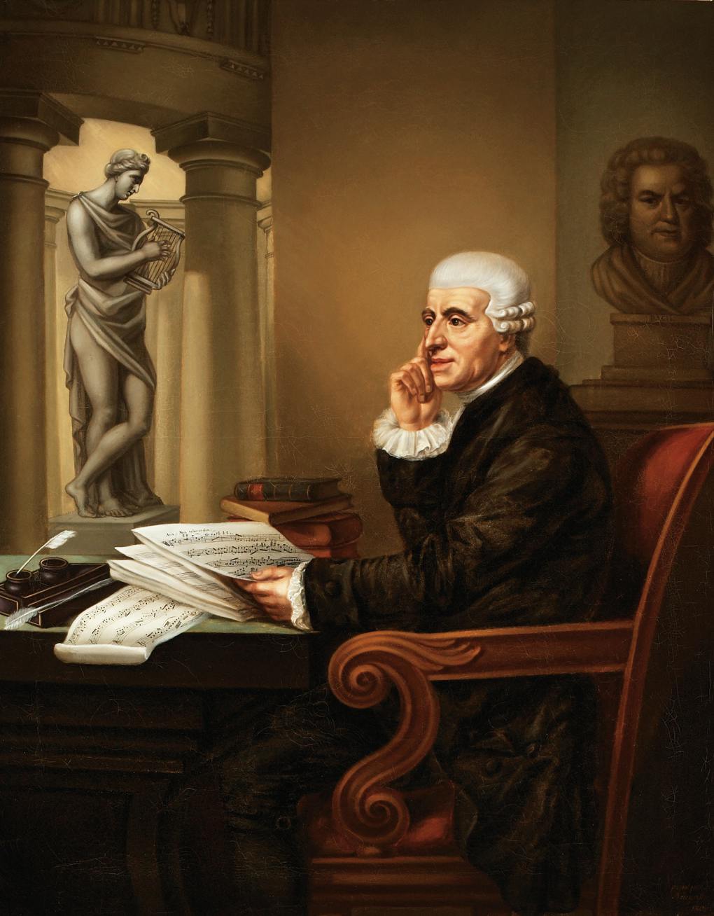 Ένας ηλικιωμένος άνδρας με λευκά μαλλιά κάθεται σε ένα γραφείο με παρτιτούρες, δείχνοντας στοχαστικός. Ένα άγαλμα στέκεται πίσω του και βιβλία στοιβάζονται κοντά του.