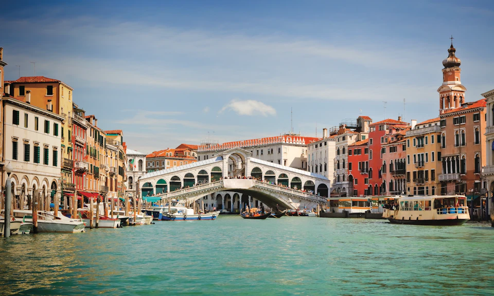 View of the Rialto Bridge over the Grand Canal in Venice, with boats and historic buildings surrounding the waterway.
