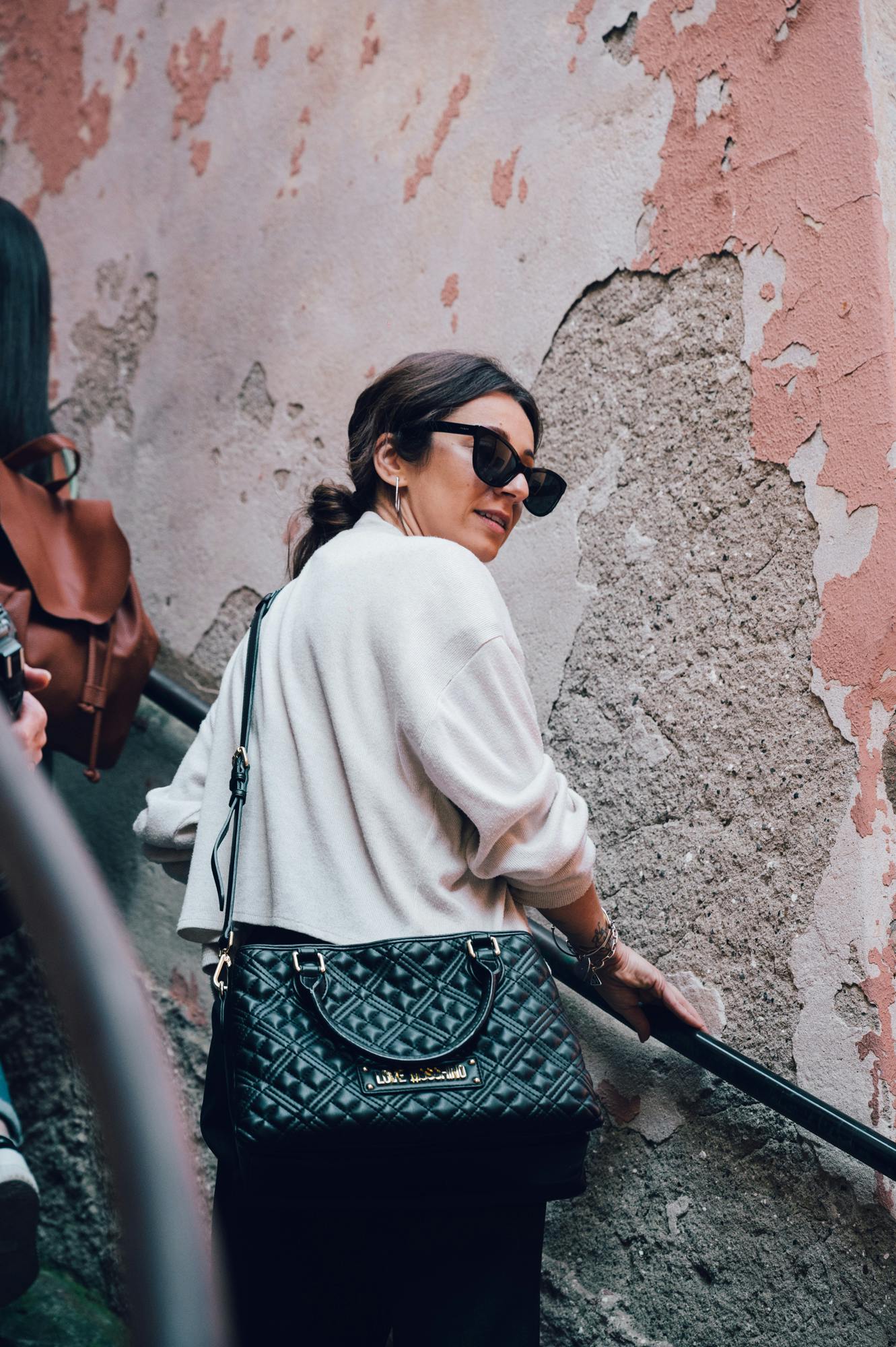 穿着太阳镜和白色毛衣的女士站在楼梯上，旁边的墙壁风化严重，油漆脱落。